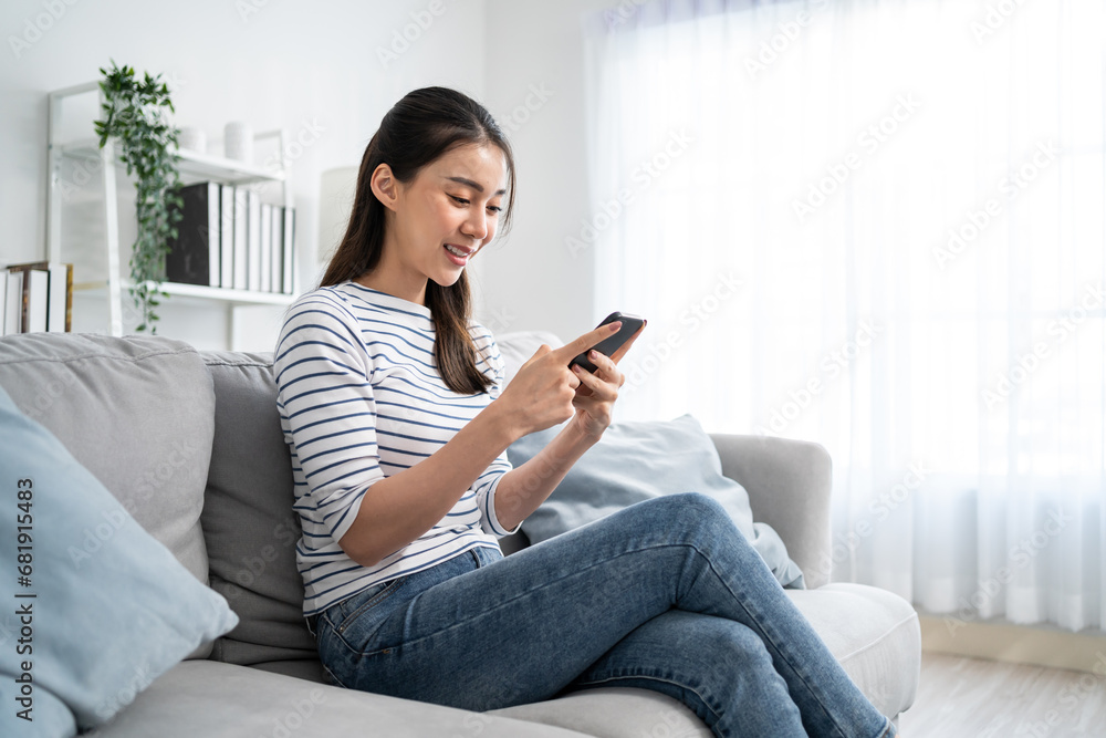 Asian beautiful woman sitting on sofa and swipe mobile phone in house. 